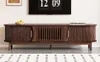 A dark brown TV stand with slatted doors and brass handles, placed in a living room setting. Produktbild-Vorschau