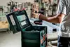 A person is holding a cordless drill over an open tool case in a workshop. Produktbild-Vorschau