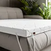 A white mattress topper is placed on a gray sofa or bed. Produktbild-Vorschau