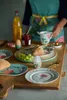 A breakfast setting with plates, food, and a person preparing a drink. Voir les images du produit