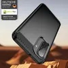 A black smartphone case with carbon fiber accents is displayed on a rocky, desert-like surface with a blurred sky background. Produktbild-Vorschau
