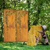 Two decorative metal screens with a floral cut-out pattern stand in a grassy garden, with a wooden lounge chair draped in a yellow blanket and a guitar leaning against it in the background. Produktbild-Vorschau