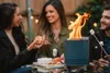 Three people are gathered around a small fire pit, roasting marshmallows and making s'mores. Produktbild-Vorschau