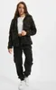 A woman is standing and posing in a studio setting, wearing a camouflage jacket and black cargo pants. Produktbild-Vorschau