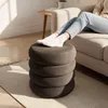 A person's legs and feet are resting on a stacked ottoman in a living room setting. Produktbild-Vorschau