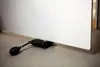 A black inflatable air wedge is placed under a white door on a concrete floor. Produktbild-Vorschau