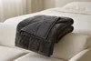 A weighted blanket is folded and draped over the armrest of a sofa, with a bed in the background. Produktbild-Vorschau