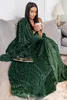A woman is sitting on a couch, wrapped in a green blanket, holding a mug. Náhled obrázku produktu