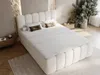 A bedroom scene with a large, upholstered bed as the focal point, decorated with pillows and a rolled bolster. The room has a textured stone wall behind the headboard and a large potted plant to the side. Produktbild-Vorschau