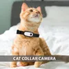 An orange cat wearing a black collar with a small camera attached, sitting on a white bed. Náhled obrázku produktu