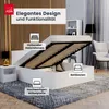 A white bed frame with the mattress lifted to reveal storage space underneath, set in a modern bedroom with a wooden accent wall and a rug. Produktbild-Vorschau