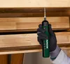 A gloved hand holds a cordless screwdriver, actively screwing into a wooden surface. Produktbild-Vorschau