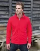 A man wearing a red fleece jacket and blue jeans stands in front of a rustic wooden wall. Produktbild-Vorschau