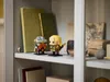 Two LEGO BrickHeadz figures are displayed on a shelf next to books and decorative items. Produktbild-Vorschau