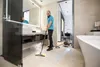 A man is using a steam cleaner in a modern bathroom. Voir les images du produit