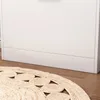 A close-up view of the bottom of a white cabinet and a round, woven rug with a circular pattern on a wooden floor. Náhľad obrázku produktu