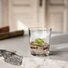 A clear glass sits on a marble countertop, filled with ice, pomegranate seeds, cucumber slices, and mint leaves, suggesting a refreshing drink. Náhľad obrázku produktu
