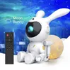 A white astronaut bunny robot sits next to a moon, with a starry sky and nebula background. A remote control is in the foreground. Náhled obrázku produktu