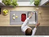 A person is using a kitchen sink with a faucet, surrounded by fruits and plants. Produktbild-Vorschau