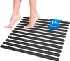 A person's feet stepping onto a set of black anti-slip strips arranged in parallel on a white surface.
