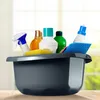 A collection of cleaning supplies in a gray basin, placed on a wooden surface with a blurred background of a window and greenery. Produktbild-Vorschau