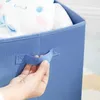 A hand is holding the handle of a blue storage basket filled with a stuffed toy. Náhled obrázku produktu