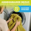 A person is holding a yellow blanket in front of an open washing machine. Produktbild-Vorschau
