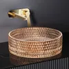 A close-up shot of a decorative glass sink and a gold faucet mounted on a dark wall. Anteprima dell’immagine prodotto