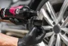A gloved hand pours liquid from a bottle onto an applicator brush, with a car wheel in the background. Anteprima dell’immagine prodotto