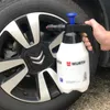 A hand holding a white pump sprayer next to a car wheel. Produktbild-Vorschau