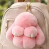 Rosa flauschiger Hasen-Schlüsselanhänger mit goldener Klammer an einem beigen Rucksack, mit grünem Laub im Hintergrund Anteprima dell’immagine prodotto