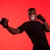 A man wearing boxing gloves and a mouthguard poses against a red background. Produktbild-Vorschau