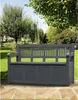 A dark gray garden bench with storage is placed on a patio in a garden setting. Produktbild-Vorschau