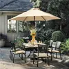 An outdoor dining set with chairs and a table under a large umbrella, surrounded by lush greenery. Produktbild-Vorschau