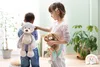 Two children are holding stuffed animals in a room with plants. Náhľad obrázku produktu