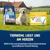 A puppy sits on grass next to a bag of dog food, with a farm building in the background and a promotional sign. Produktbild-Vorschau