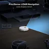 A white robot vacuum cleaner is shown on a tiled floor, with a blue light beam emanating from it, indicating its navigation system. The background features furniture and a beanbag chair, suggesting a home environment. Produktbild-Vorschau