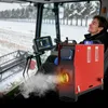A person is sitting in a combine harvester cab in a snowy field, with a red heater unit in the foreground emitting steam. Produktbild-Vorschau