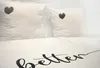 A close-up view of a white duvet cover with black text and two white pillows with black heart designs. Produktbild-Vorschau