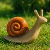 A ceramic garden decoration in the shape of a snail sitting on grass. Voir les images du produit
