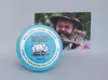 A tin of Reuzel pomade is placed in front of a photograph of a man. Produktbild-Vorschau