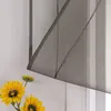 A close-up of a dark gray sheer curtain with sunflowers in the foreground. Produktbild-Vorschau