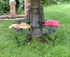 A round metal bench around a tree in a garden, with a hat and a bag on it. Náhled obrázku produktu