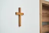A wooden cross is mounted on a white wall next to a wooden door. Podgląd zdjęcia produktu