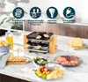 A raclette grill set up on a kitchen counter with various food items like cheese, bread, salami, and asparagus. Produktbild-Vorschau