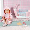 A baby doll is sitting next to a pink toy bathtub in a bathroom setting. Produktbild-Vorschau