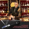 A man in a suit pours liquor into a glass behind a bar, with bottles on shelves in the background. A refractometer is in the foreground. Produktbild-Vorschau