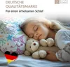 A young girl sleeping peacefully with a teddy bear, on a pillow with a colorful pattern. The German flag is shown in a heart shape. Produktbild-Vorschau