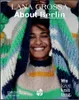 A woman smiling and holding up a colorful knitted sweater. Produktbild-Vorschau
