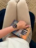 A person is sitting down, holding a book and wearing a smartwatch. Anteprima dell’immagine prodotto